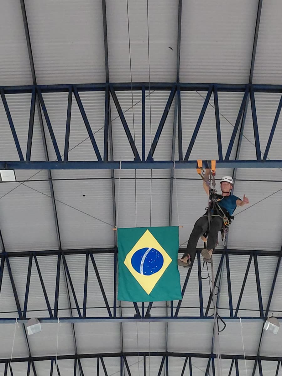 Técnico suspenso na treliça ao lado da bandeira do Brasil