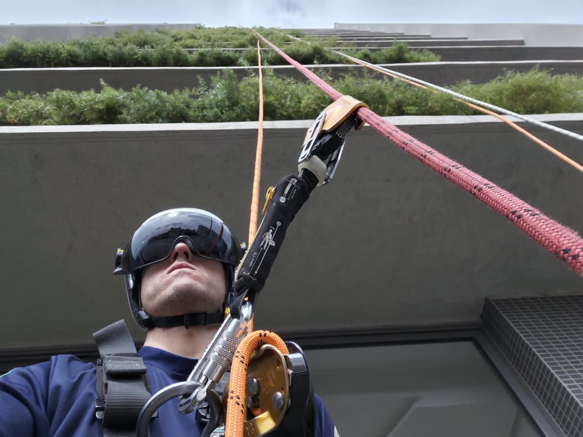 Técnico subindo pelas cordas junto às floreiras da fachada