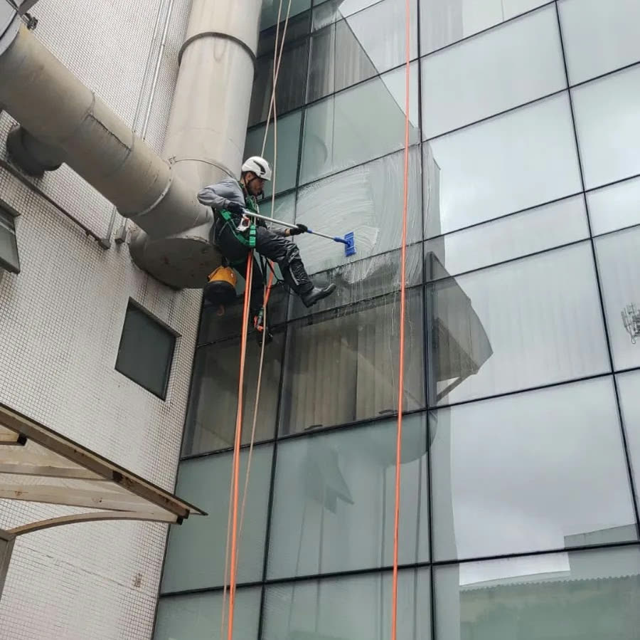 Técnico limpando vidro de fachada com rodo, em acesso por cordas