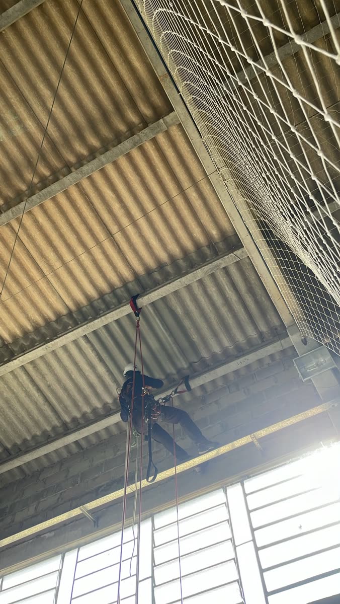 Técnico ancorado na estrutura da cobertura do galpão