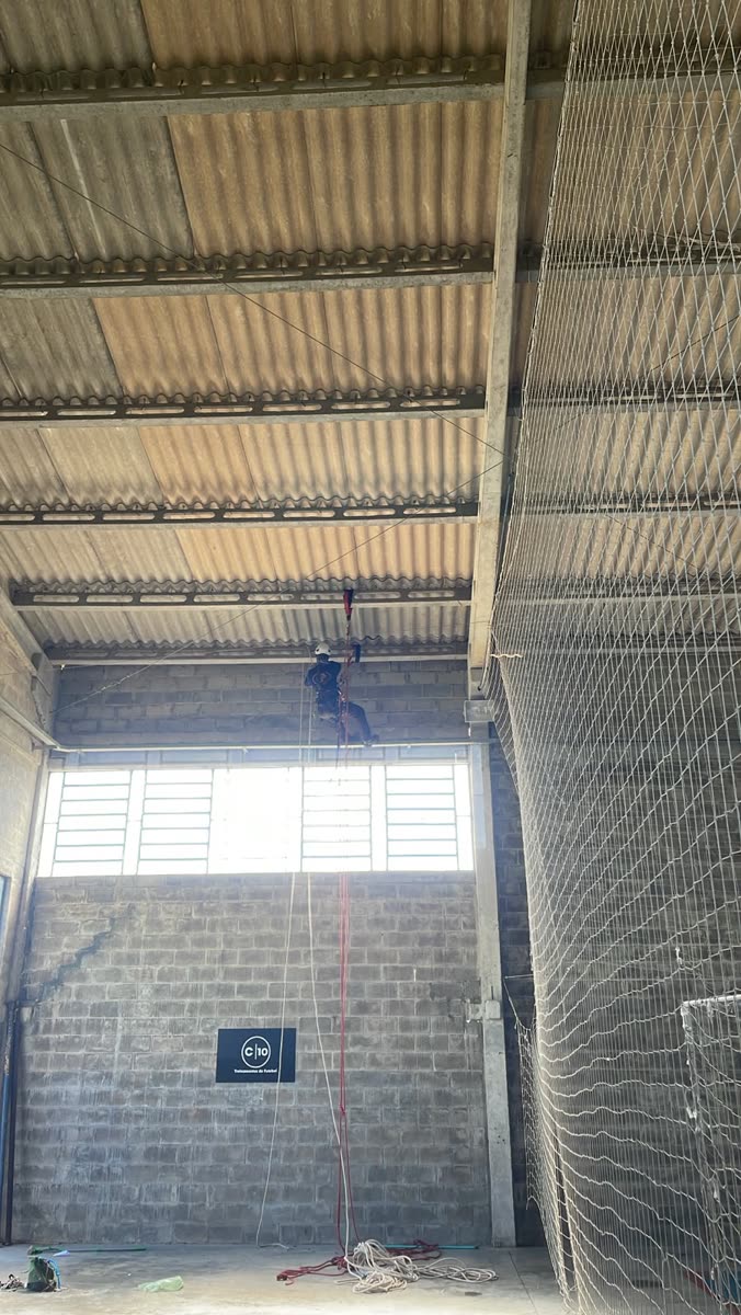 Técnico suspenso na cobertura de galpão ao lado da rede de proteção